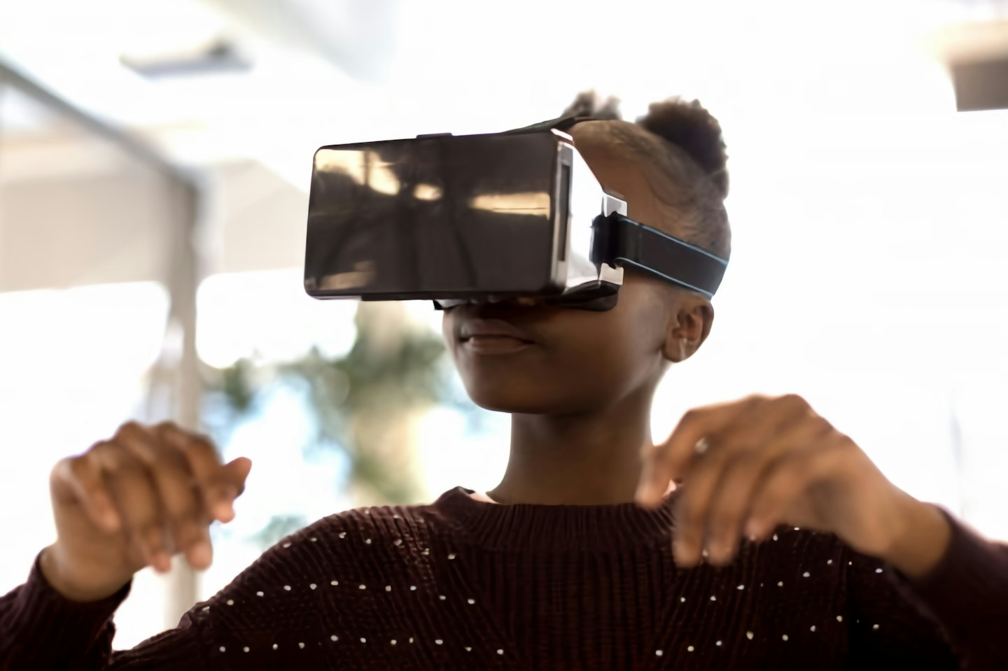 Giovane persona con visore VR, alza le mani con entusiasmo.